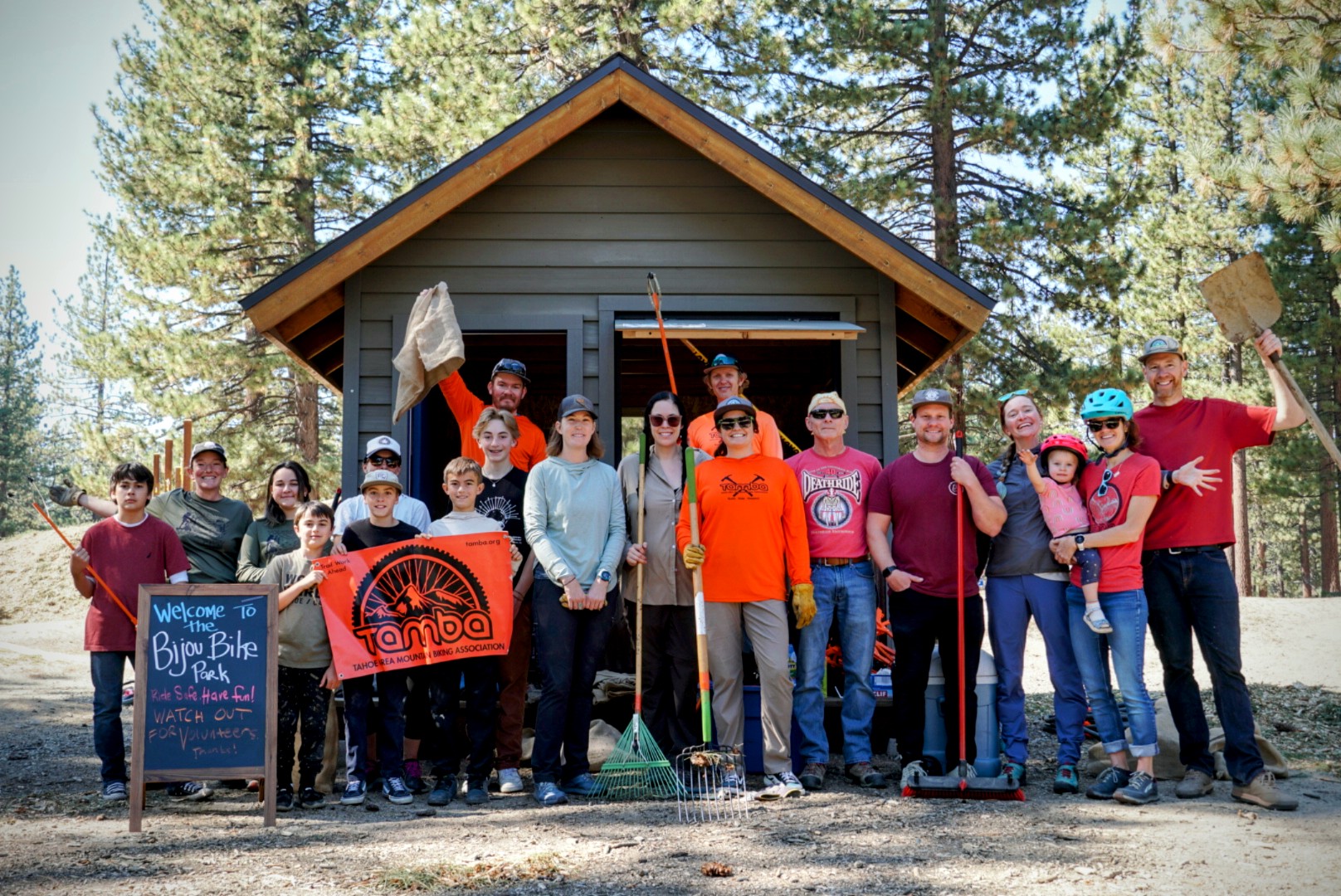A group of people, some in bike helpments, some with tools, posing in front of a shed.