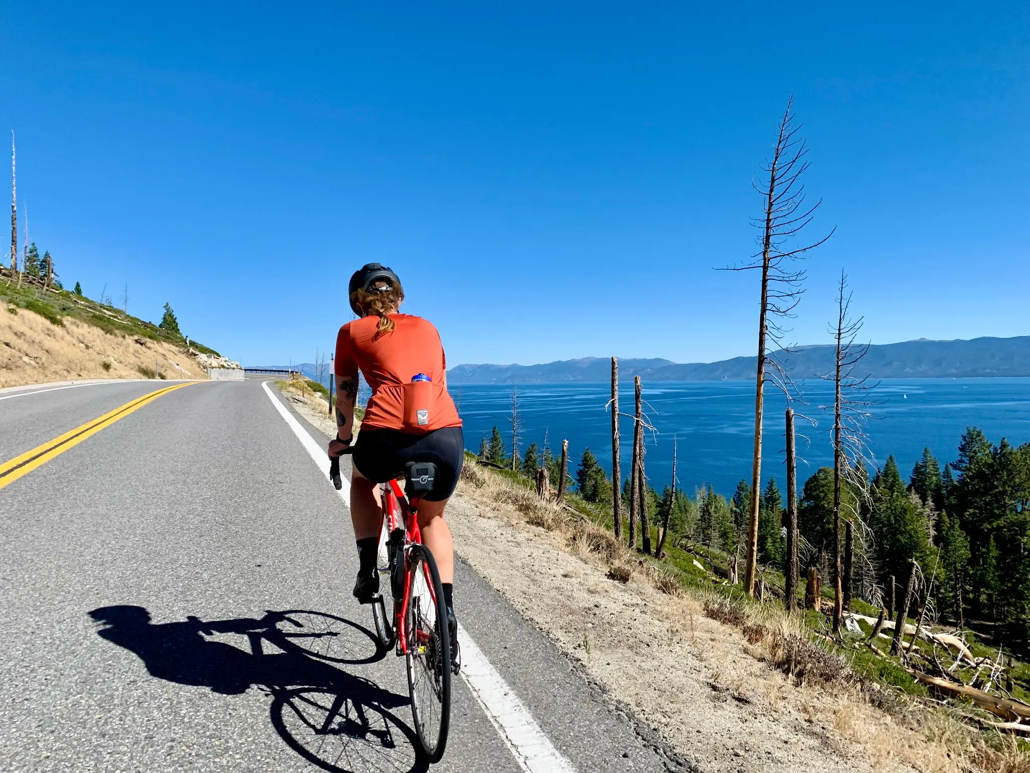 A cyclist riding a bike up a steep road with a large lake to their right.