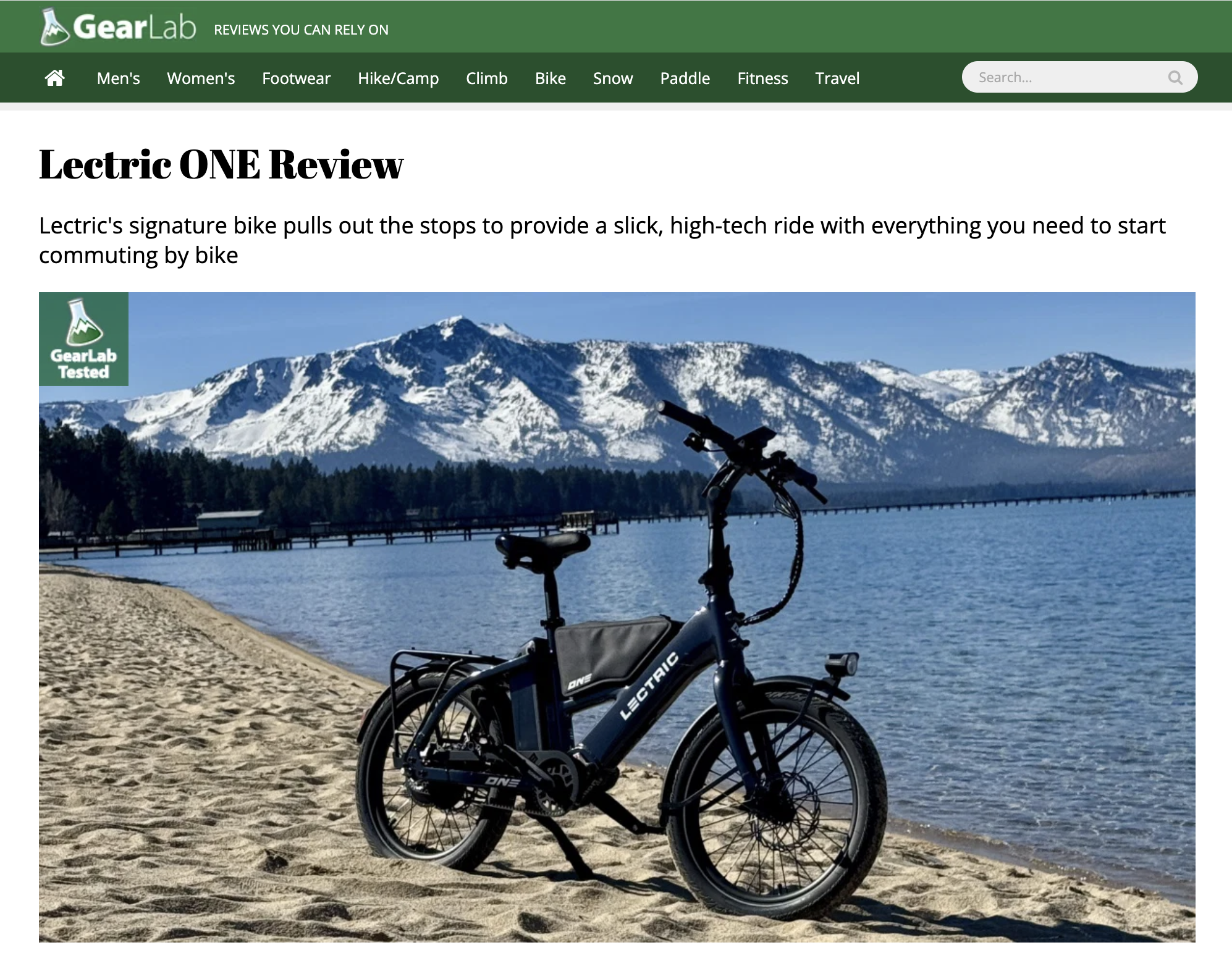 A Lectric One e-bike on a sidewalk surrounded by pine trees.